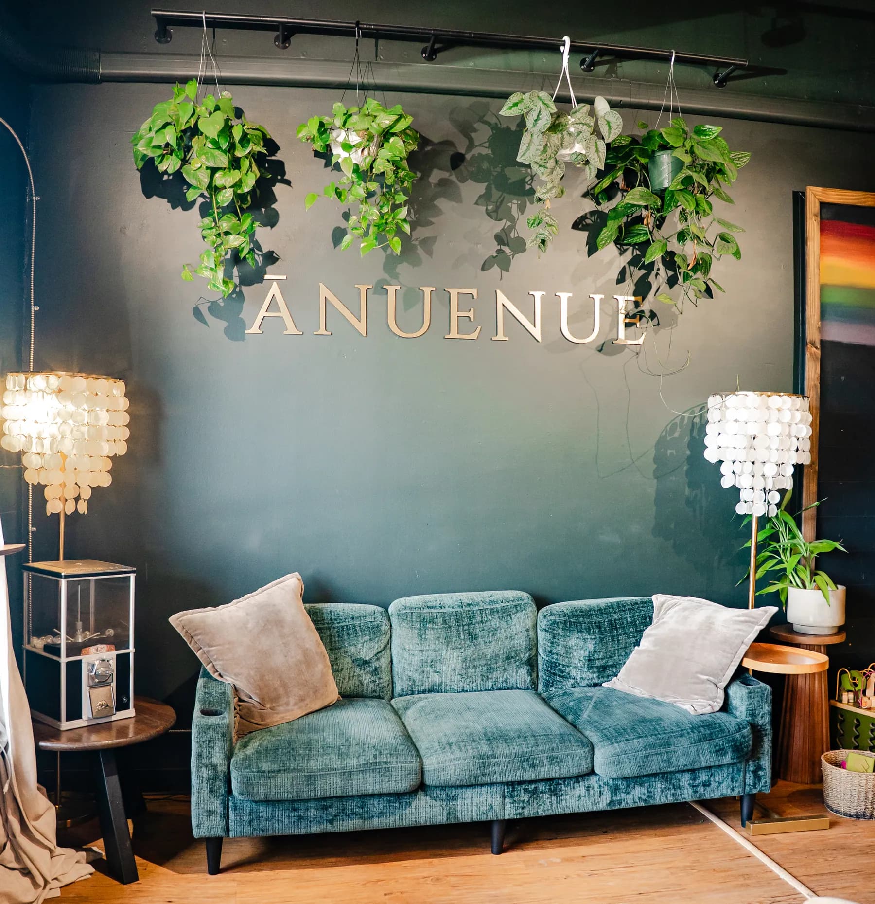 The Ānuenue lounge with its teal velvet couch, plants, and brass lettering, ready for a gathering